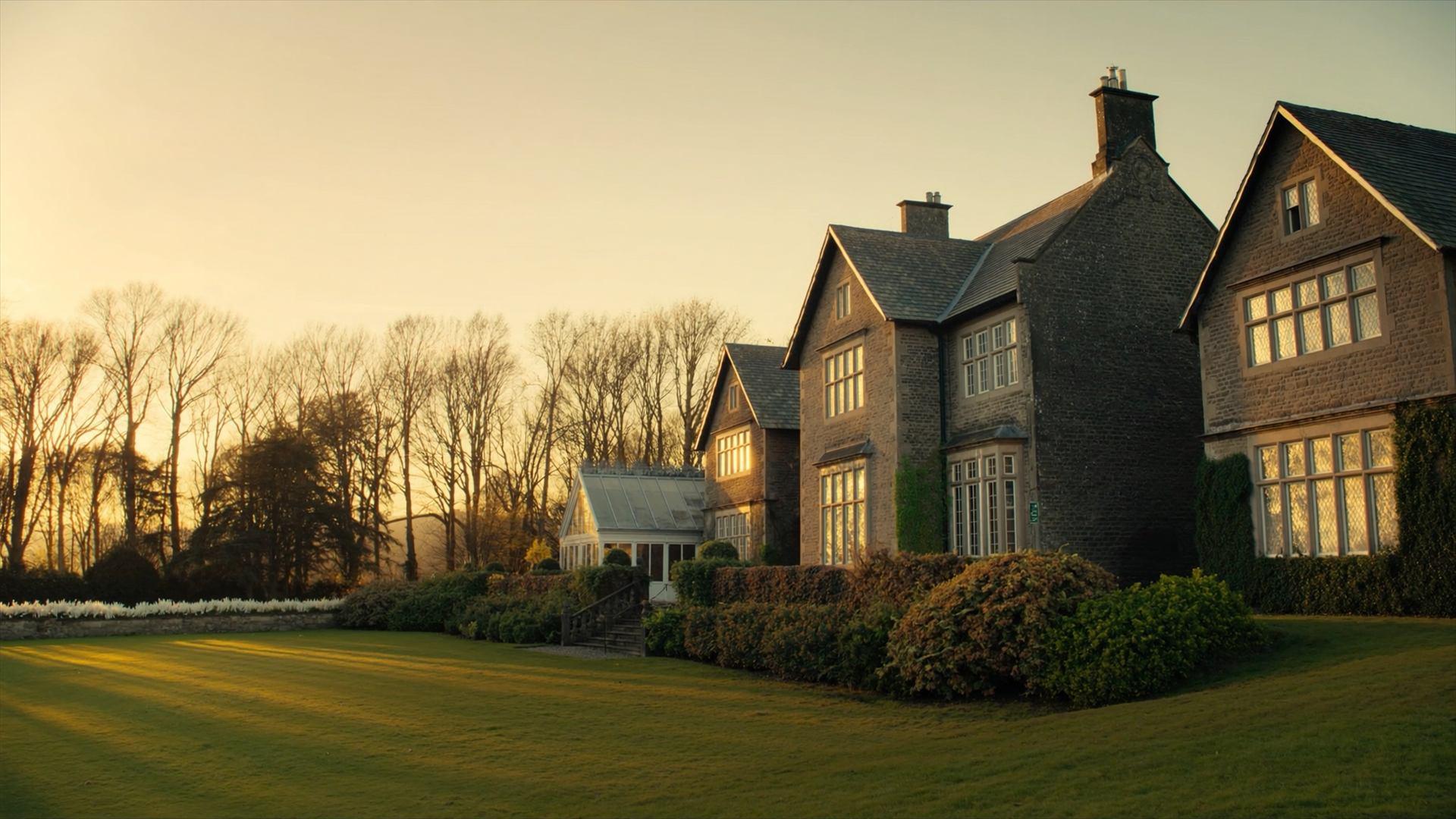 The west front and lawn raked by low golden sunlight, long shadows from a line of lime trees