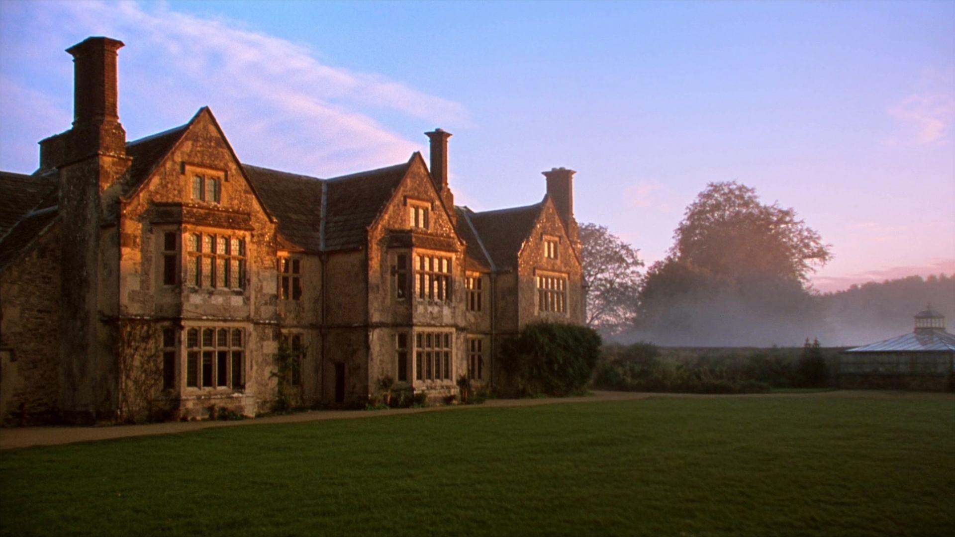 Wrenfell Hall at first light, low sun warming the stone front and mist lying over the parkland behind