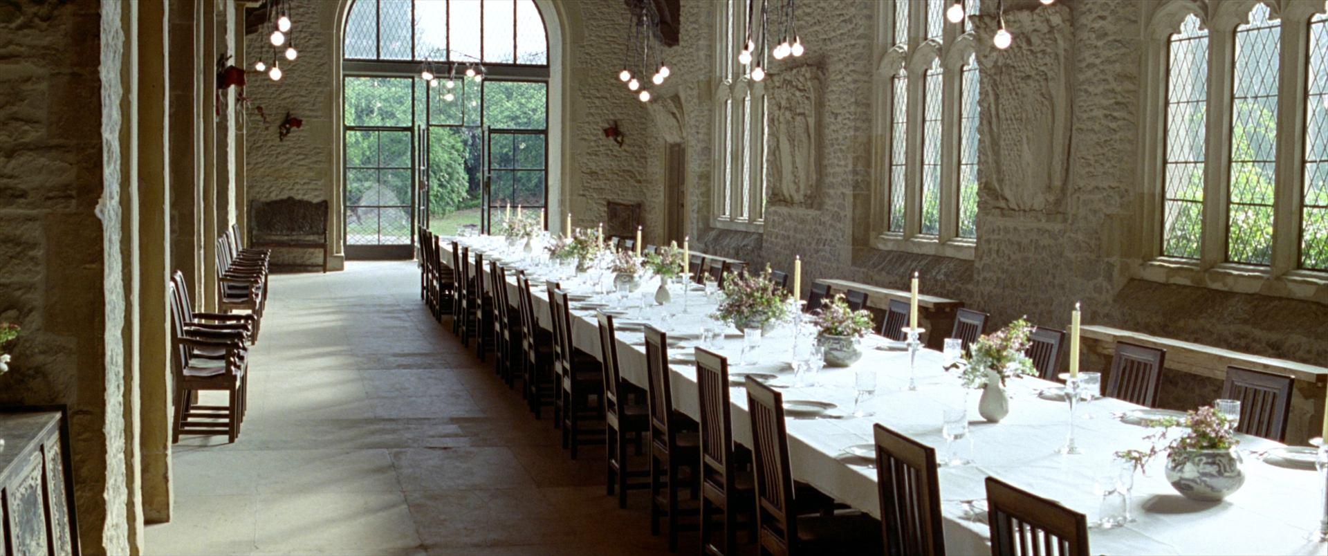 One long oak table set for eighty with white linen and candles, tall windows down one side